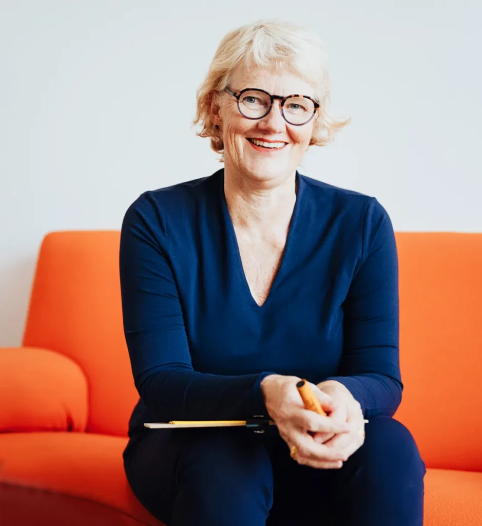 Wirtschaftspsychologin und Mentorin Jutta Grebing sitzt auf einer orangen Couch und lacht